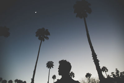 Low angle view of silhouette man and palm trees against clear sky