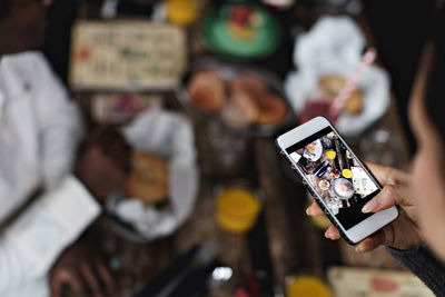 Cropped image of woman photographing food on dining table at restaurant