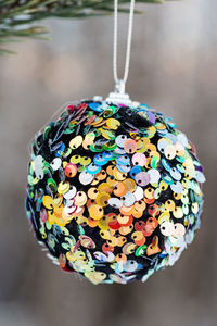 Hanging multi colored glitter christmas ball on spruce and over blurred background