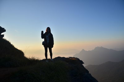 Full length of woman standing on mountain against clear sky during sunset