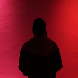 Rear view of silhouette man standing against red wall