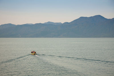 Person in boat on sea against mountain range