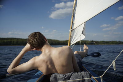 Rear view of shirtless man sitting in boat on sea against sky