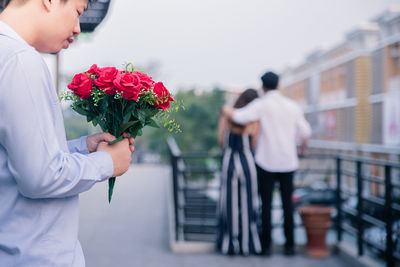 Rear view of people holding red rose standing against wall