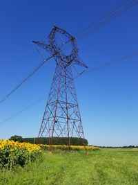 Low angle view of electricity pylon on field against clear blue sky