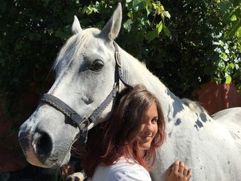 Portrait of teenage girl embracing horse against trees