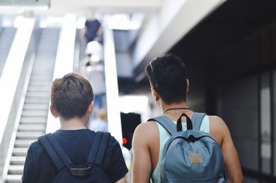 Rear view of boys with backpacks standing against escalator