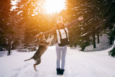 Dog playing with woman on snow covered field during sunrise
