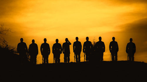 Silhouette army soldiers standing in row against sky during sunset