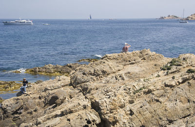 Man and boy sitting on rock formation at french riviera