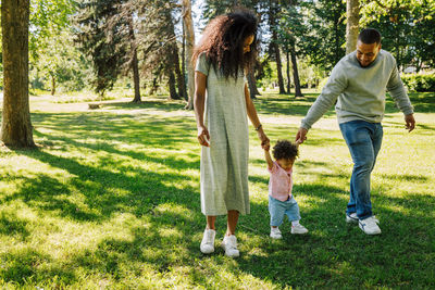 Parents holding hands with toddler son while walking at park