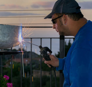 Mid adult man welding metal by railing during sunset