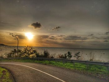 Road by sea against sky during sunset