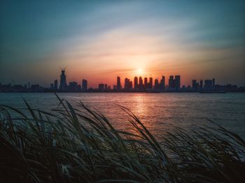 Scenic view of sea by buildings against sky during sunset