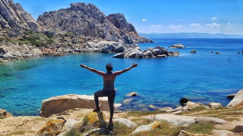 Rear view of man standing on rock by sea against sky