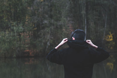 Rear view of man wearing hooded shirt by lake in forest