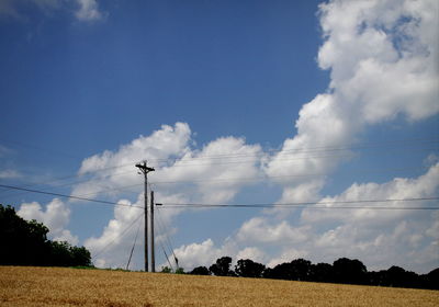 Low angle view of agricultural field against sky with power lines