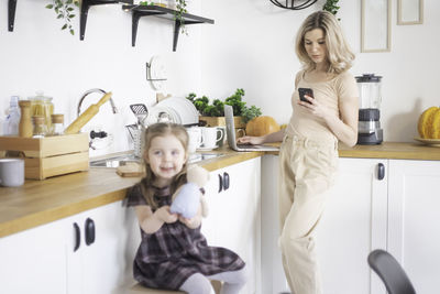 Mother using mobile phone while daughter playing with toy at kitchen