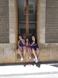 Full length portrait of siblings eating flavored ice while sitting by window