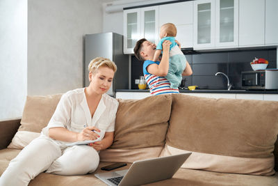 Mother working on laptop while kids playing in kitchen at home