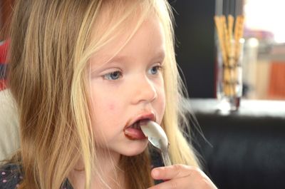 Close-up of cute girl eating ice cream with spoon at restaurant