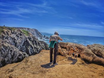 Rear view of man standing on rock by sea against sky