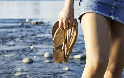 Midsection of woman holding flip-flop at beach