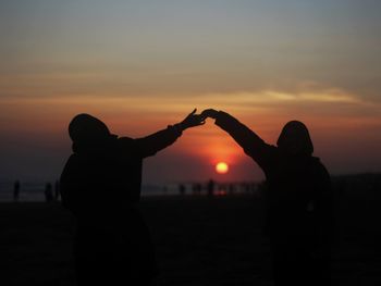 Silhouette couple holding hands against orange sky during sunset