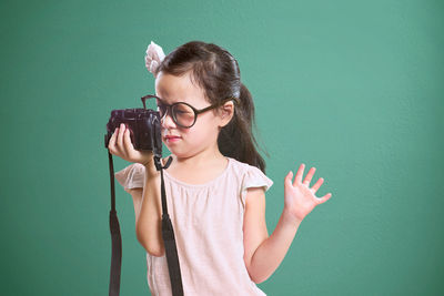 Cute girl holding camera while standing against colored background