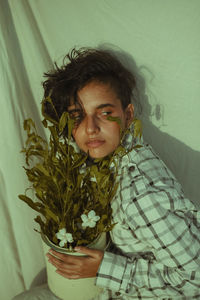 Portrait of young man with potted plant against wall