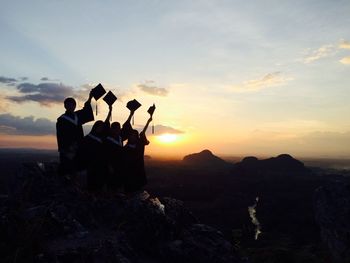 People in graduation gown on mountain against sky during sunset