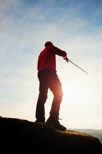 Tourist in windcheater with sporty trecking poles in hands stand on rocky view point. spring weather