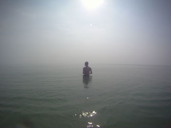 Shirtless man standing in sea against sky