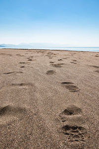 Footprints on sand at beach against clear sky