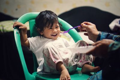 Cropped hand of person feeding food to baby girl at home