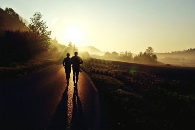 People walking on road against sky during sunrise