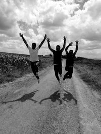 Friends jumping with arms raised against sky