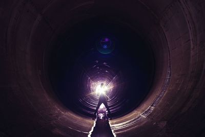 Full length of person with lighting equipment standing in sewage tunnel