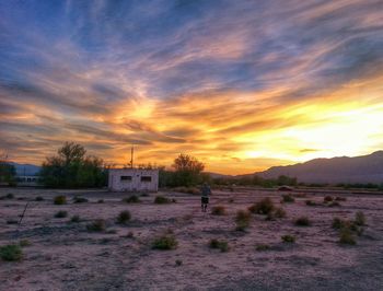 Scenic view of landscape against cloudy sky at sunset