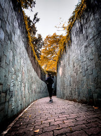 Rear view of man walking on footpath amidst wall