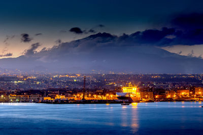 Illuminated buildings by sea against sky at night