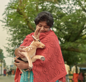 Full length of woman standing outdoors, affectionately holding a soft toy version of deer cub. 