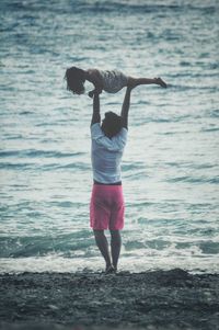 Rear view of father lifting daughter at beach