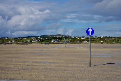 Road sign on beach against sky