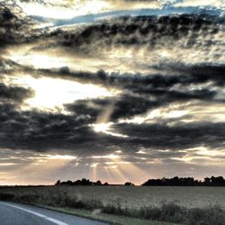 Road passing through field against cloudy sky