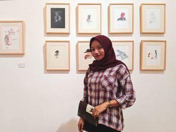 Portrait of smiling young woman standing against wall