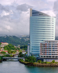 Modern buildings by river against sky in city