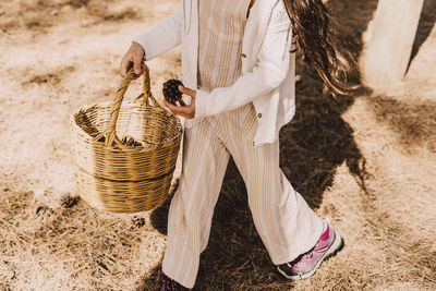 Elementary girl collecting pine cones in wicker basket at park