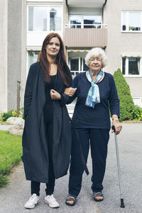 Full length portrait of young woman standing with grandmother outside house