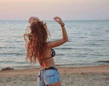 Young woman standing at beach against sky during sunset